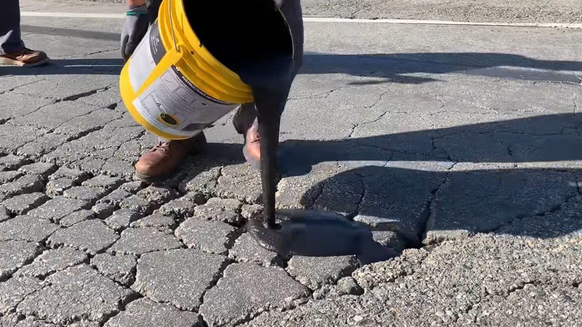 Pouring FastPatch ACR polymer onto alligatored asphalt
